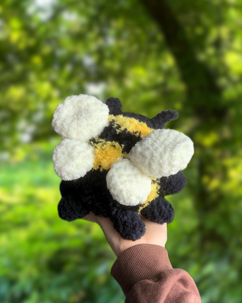 May include: A crocheted bumble bee plush toy with black and yellow stripes and white fuzzy wings.