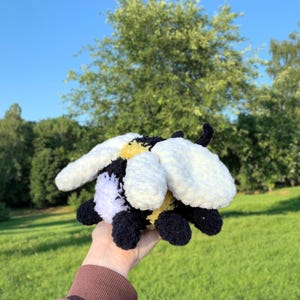 May include: A crocheted plush bee toy with black, white, and yellow yarn. The bee has a fuzzy texture and is holding its wings out.