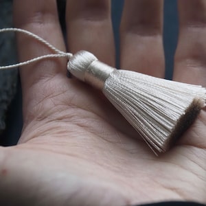 May include: A white tassel with a loop for hanging. The tassel is made of soft, silky fibres and is approximately 5 cm long.