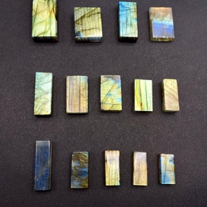 May include: A collection of 15 polished labradorite stones, each cut into a rectangular shape. The stones are a mix of green, blue, and gold colours with iridescent shimmer.