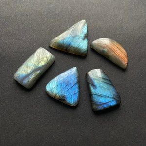 May include: Five iridescent labradorite gemstone cabochons in various shapes, including a triangle, rectangle, and half-circle. The stones have a blue-green and gray color with a shimmery effect.