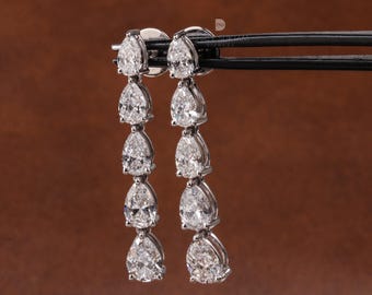 May include: A pair of elegant drop earrings featuring multiple pear-shaped, clear gemstones. The earrings are set in a silver-colored metal and are suspended from a post. The gemstones are arranged in a cascading design, creating a sparkling effect.