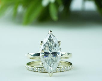 May include: A marquise-cut diamond engagement ring with a matching band. The engagement ring features a large, clear marquise-shaped diamond set on a gold band. The matching band is also gold and is encrusted with small diamonds.