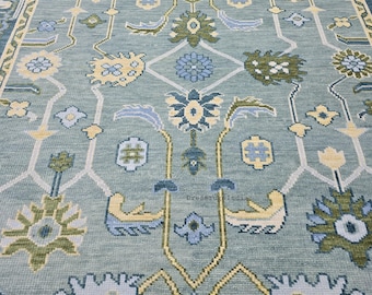 May include: A close-up of a light blue rug with an intricate floral pattern. The design features various floral motifs in shades of yellow, green, and blue, set against a light blue background. The rug has a detailed, textured appearance.