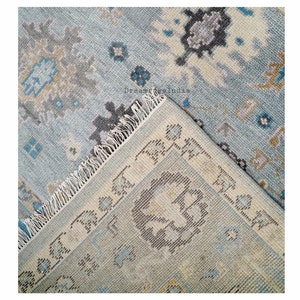 May include: Close-up of a blue and cream patterned rug with fringed edges. The rug has a traditional design with floral motifs.