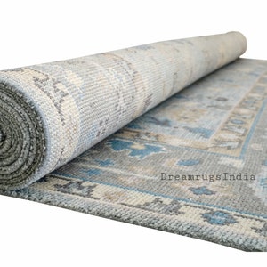 May include: A rolled up blue and beige patterned rug with a gray backing. The rug has a traditional design with floral motifs. The text "Dreamrugs India" is visible on the rug.