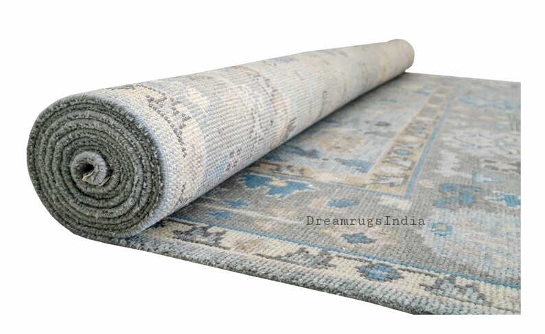 May include: A rolled up blue and beige patterned rug with a gray backing. The rug has a traditional design with floral motifs. The text "Dreamrugs India" is visible on the rug.
