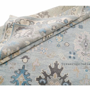 May include: A light blue rug with a traditional Persian design. The rug has a faded look and features intricate patterns in shades of blue, beige, and gray. The rug is folded in half, revealing the fringe on the edges. The text "DreamrugsIndia" is visible in the bottom right corner.