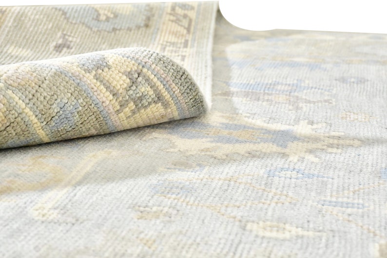 May include: A light blue rug with a subtle pattern of white and beige. The rug is rolled up, showing the edge of the rug with a more detailed pattern.