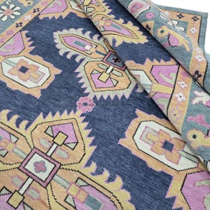 May include: A blue, pink, and yellow patterned rug with a geometric design. The rug is folded in half, showing the pattern on both sides.