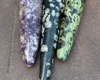 May include: Three polished stone wands. The wands are cylindrical with rounded ends. One is purple and white, one is black with white spots, and the third is green and brown.