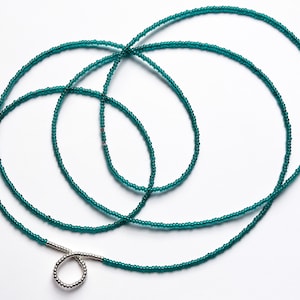 Könnte beinhalten: Eine türkisfarbene Perlen-Taillenkette mit einem silbernen Verschluss. Die Kette besteht aus kleinen, runden Perlen und ist etwa 100 cm lang.