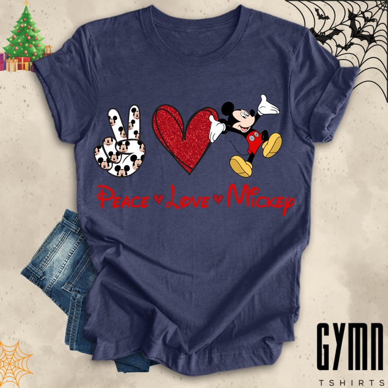 Pode incluir: Uma camiseta azul marinho com um sinal de paz feito de rostos do Mickey Mouse, um cora&ccedil;&atilde;o vermelho de glitter e o Mickey Mouse com uma roupa vermelha e amarela. O texto "Peace Love Mickey" est&aacute; impresso em vermelho abaixo do design.
