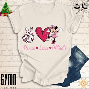 Pode incluir: Camiseta branca com um sinal de paz rosa, um cora&ccedil;&atilde;o e um gr&aacute;fico de Minnie Mouse. O texto "Peace Love Minnie" &eacute; impresso abaixo do gr&aacute;fico.