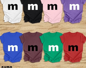 May include: Eight t-shirts with the letter "m" printed on the front. The shirts are in different colors: white, black, pink, purple, blue, maroon, green, and red.