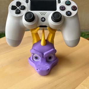 Può includere: Un supporto per controller PlayStation 4 a forma di testa di drago, stampato in 3D, di colore viola e giallo.