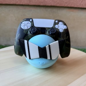 May include: A blue and white camouflage PlayStation 5 controller with a light blue and white striped visor on top of a light blue egg-shaped object.