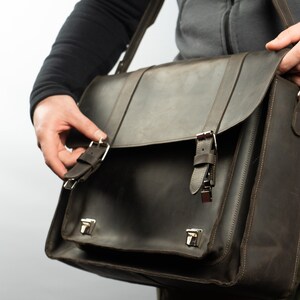 Peut inclure: Un sac messager en cuir brun avec deux boucles et une fermeture &agrave; rabat. Le sac a une bandouli&egrave;re et se porte sur l'&eacute;paule.