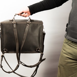 Peut inclure: Une mallette en cuir marron avec des bretelles r&eacute;glables qui peuvent &ecirc;tre port&eacute;es comme un sac &agrave; dos. Le sac a une poign&eacute;e sup&eacute;rieure et une poche avant.