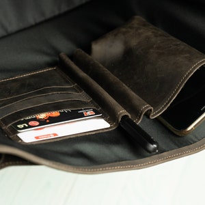 Peut inclure: Un sac en cuir marron avec plusieurs poches, dont une grande poche pour un t&eacute;l&eacute;phone, une petite poche pour les cartes et un porte-stylo.