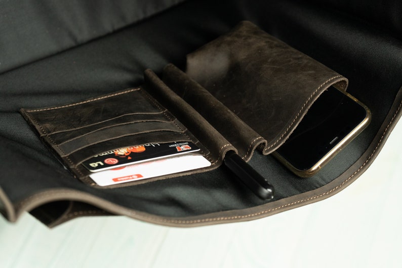 Peut inclure: Un sac en cuir marron avec plusieurs poches, dont une grande poche pour un t&eacute;l&eacute;phone, une petite poche pour les cartes et un porte-stylo.