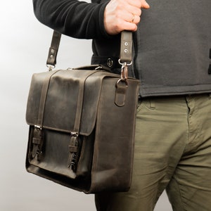 Peut inclure: Un sac messager en cuir brun avec une longue sangle r&eacute;glable. Le sac a deux boucles sur le devant et une fermeture &agrave; rabat.