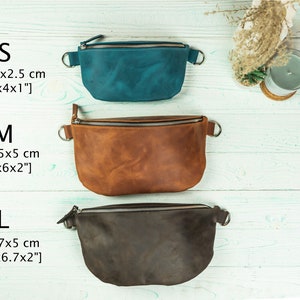 K&ouml;nnte beinhalten: Drei Leder-Bauchtaschen in den Farben T&uuml;rkis, Braun und Dunkelbraun, jeweils mit Rei&szlig;verschluss und Metallring an jeder Seite. Gr&ouml;&szlig;en: S (20x10x2,5 cm), M (25x15x5 cm), L (29x17x5 cm).