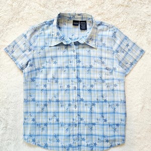 May include: A short-sleeved button-down shirt in a blue and white plaid pattern, adorned with embroidered floral designs. The shirt features a collared neckline and is made of a lightweight fabric, suitable for casual wear.