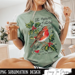 May include: A green t-shirt with a robin bird, holly leaves, and red berries. The text on the shirt reads "Let Heaven & Nature Sing, Jesus is the reason".
