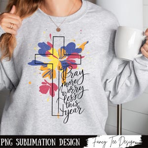 May include: A sublimation design featuring a black cross with a colorful floral design behind it. The text "Pray more worry less this year" is written in black cursive lettering.