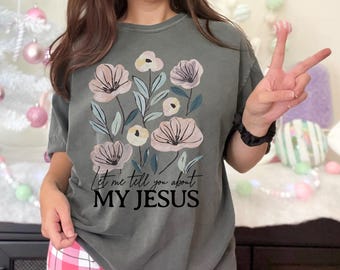 Puede incluir: Una camiseta gris con un diseño floral y el texto "Let me tell you about MY JESUS".
