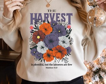 May include: A beige sweatshirt with the text "THE HARVEST is plentiful, but the laborers are few Matthew 9:37" and a floral design with purple, orange, red, and white flowers.