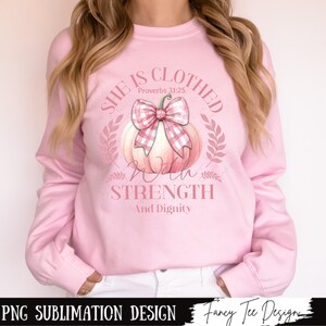 May include: Pink sweatshirt with a graphic design of a pink and white pumpkin with a bow and the text "She is clothed with strength and dignity" and "Proverbs 31:25".