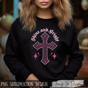 Puede incluir: Una sudadera negra con una cruz de brillantes rosados y el texto "Shine and Bright" en una fuente gótica.