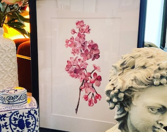Può includere: Un dipinto ad acquerello incorniciato di un ramo di fiori rosa con petali delicati. Il dipinto è esposto su un tavolo accanto a un busto in ceramica bianca.