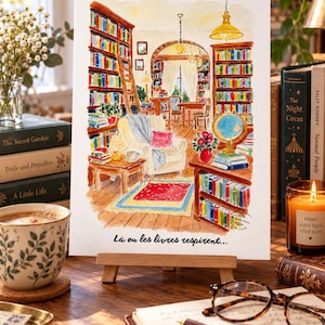 Może przedstawiać: Akwarelowa ilustracja na drewnianej sztaludze przedstawiająca wnętrze przytulnej biblioteki z regałami na książki, wygodnym fotelem, globusem i dywanem. Na dole znajduje się napis "L&agrave; ou les livres respirent...".