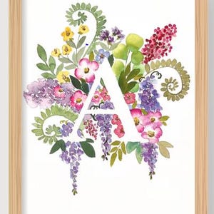 May include: Watercolor floral art print featuring the letter "A" in white, surrounded by a vibrant arrangement of pink, purple, yellow, and green flowers and foliage. The artwork is framed in a light brown wooden frame.