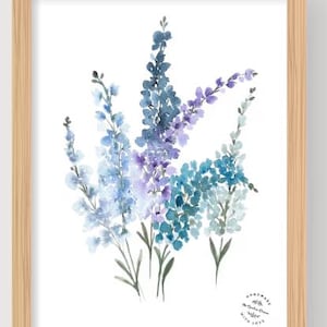 May include: Watercolor painting of blue and purple flowers in a wooden frame. The artwork features a cluster of delicate blooms in shades of blue, teal, and purple against a white background. The frame is a light wood color.