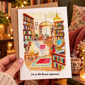 Może przedstawiać: Akwarelowa kartka okolicznościowa przedstawiająca przytulną bibliotekę z wysokimi regałami, wygodnym fotelem, globusem i małym stolikiem. Tekst na dole kartki brzmi "L&agrave; ou les livres respirent..." i jest napisany czarną kursywą.