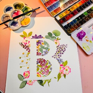 May include: A watercolour painting of the letter "B" created using a range of flowers in shades of pink, purple, white, and green.