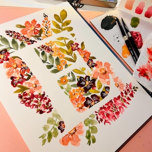 Pu&ograve; includere: Dipinto ad acquerello della lettera "E" decorata con fiori arancioni, rossi e bordeaux e foglie verdi. Una scatola di metallo di acquerelli e una tavolozza con pennelli sono sullo sfondo. L'opera d'arte &egrave; su carta bianca.