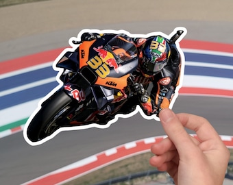 May include: A black and orange motorcycle with a rider wearing a helmet and racing suit. The motorcycle has the number 33 on the side and the word "KTM" on the front. The motorcycle is on a sticker with a white border.