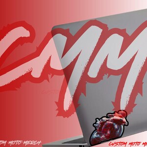May include: A white laptop with a red and white graphic that says "CYM" and a sticker of a red motorcycle on the bottom right corner. The text "CUSTOM MOTO MERCH" is at the bottom of the image.