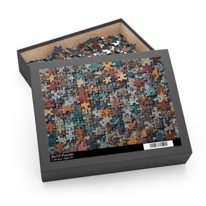Puede incluir: Un rompecabezas parcialmente ensamblado en una caja negra. Las piezas son de varios colores, incluyendo tonos de marrón, azul y verde. La caja está etiquetada como "8x10 Puzzle" con "120 piezas Edades 9+".