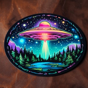 Puede incluir: Una ilustración colorida de un platillo volante flotando sobre un bosque por la noche. El platillo es rosa, morado y azul con un rayo de luz que brilla hacia abajo. El bosque es verde oscuro y el cielo es negro con estrellas.