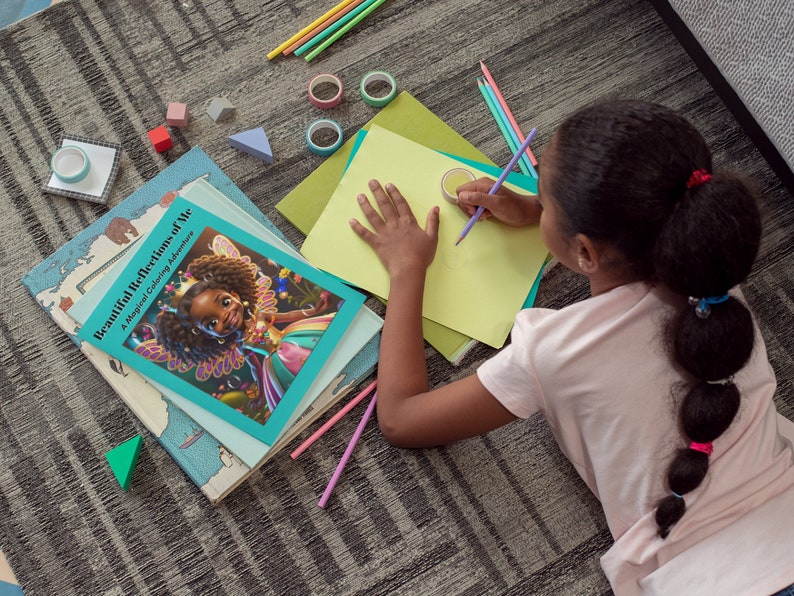 May include: A young person is coloring on a sheet of yellow paper with a purple pencil. The person is lying on a gray carpet with a book titled "Beautiful Reflections of Me: A Magical Coloring Adventure" on the floor next to them.
