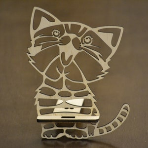 May include: A wooden cat-shaped shelf with a light brown finish. The cat has a detailed design with cut-out features, including eyes, stripes, and a tail. The shelf is designed to hold small items.