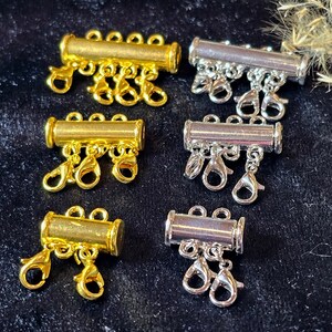 Könnte beinhalten: Sechs goldene und silberne Metall-Verbindungsverschlüsse für die Schmuckherstellung. Jeder Verschluss hat drei oder vier Schlaufen zum Anbringen von Ketten oder Schnüren.