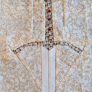 May include: A white fabric sword with a brown and red fabric handle. The sword is made using a patchwork technique.