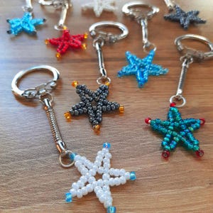 Peut inclure: Un ensemble de porte-clés en forme d'étoile en perles de différentes couleurs, notamment bleu, rouge, vert, blanc et noir. Chaque porte-clés est orné d'un charme en forme d'étoile avec un anneau argenté.